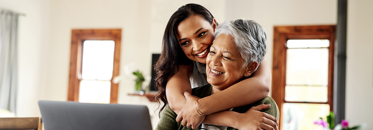 Woman on computer with another woman hugging her while looking over her shoulder